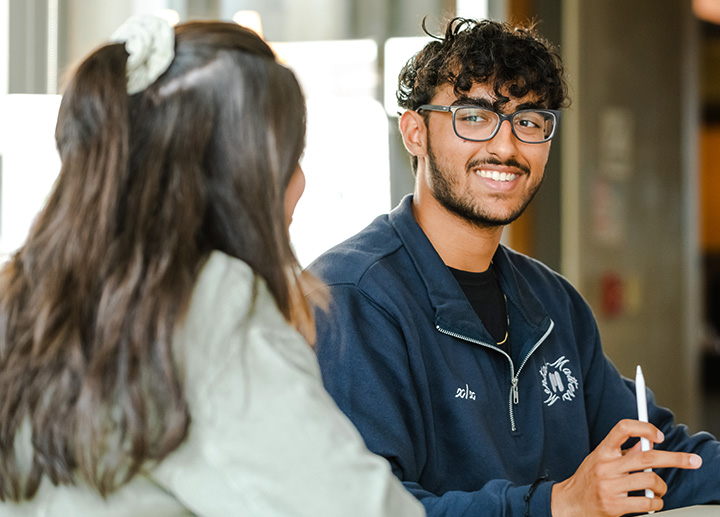 A student smiling as another is talking to him